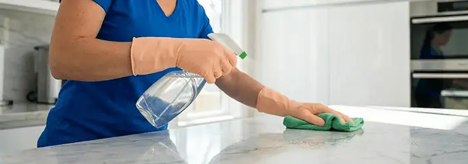 Maid service worker spraying and wiping a kitchen countertop with a microfiber cloth for sanitizing, Lakeland, FL.