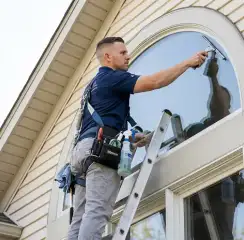 Professional window cleaner on a ladder using a squeegee to clean an exterior arched window, Lakeland, FL.