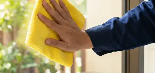 House cleaner wiping a glass window with a yellow microfiber cloth for streak-free cleaning, Lakeland, FL.